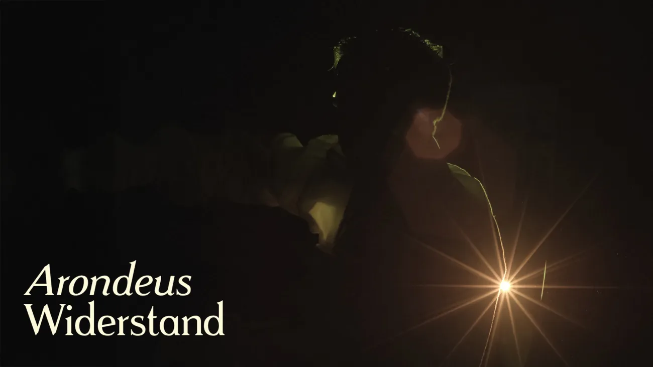 Image showing the silhouette of a dancer in a costume in front of a bright light, titled „Arondeus Widerstand“. 